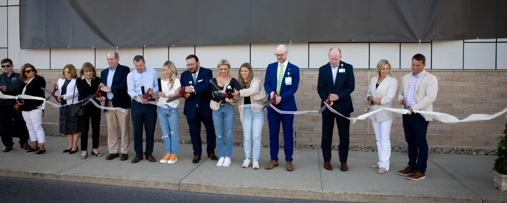 People with pairs of giant scissors stand in a line to cut a big ribbon.