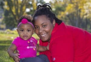 A young mom and her new baby lay in the meadow of a park together.
