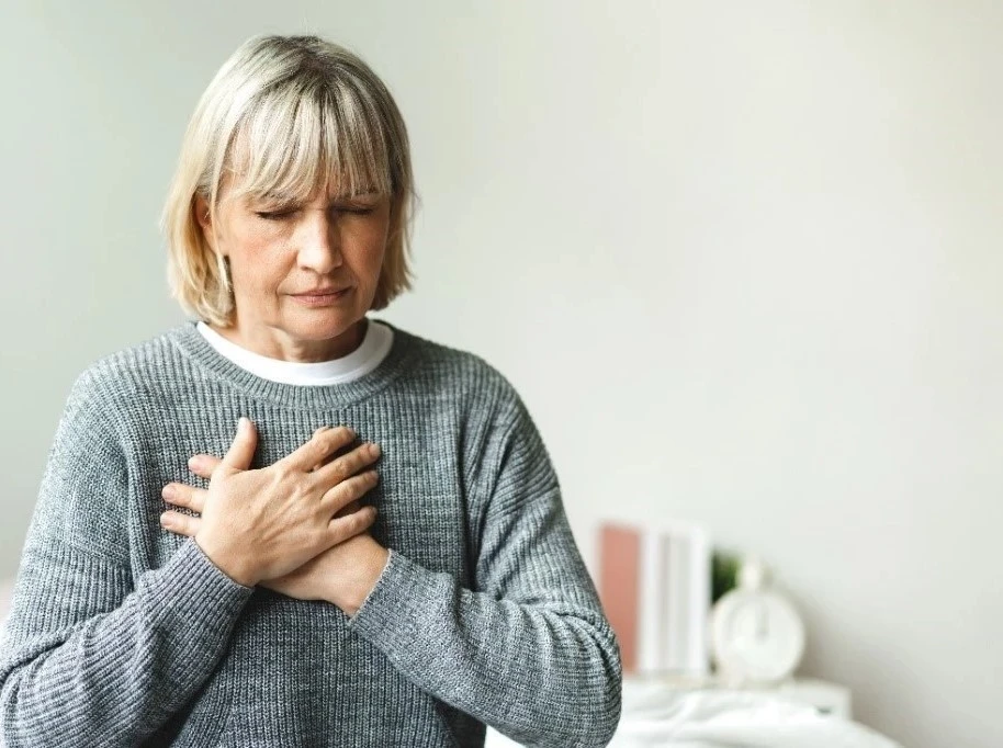 A senior woman clutches her chest in pain.