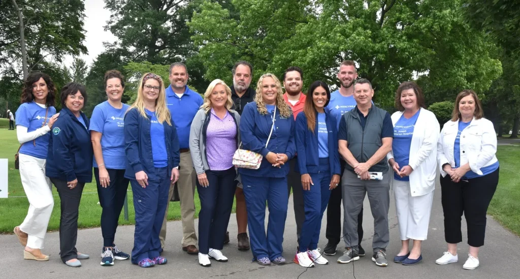 Event workers for St. Joseph Warren Hospital's 100th Anniversary Golf Outing pose together for a picture outside, beneath some trees.