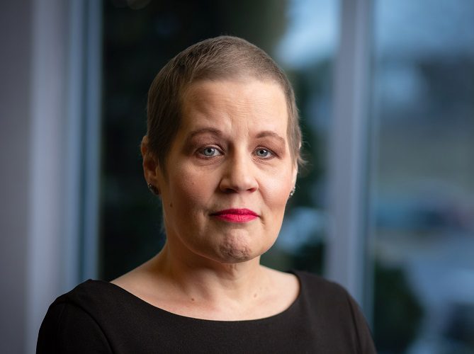 A woman with close-cropped hair stands in a hospital hallway.