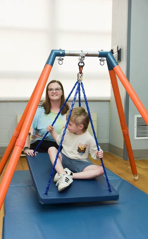 A occupational therapist works with a smiling five-year-old boy.