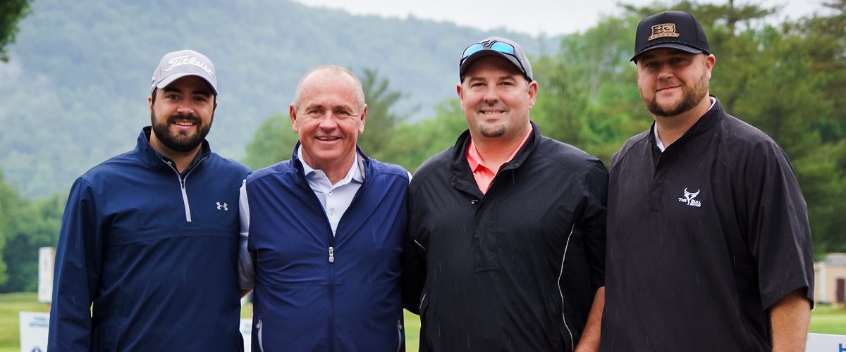 Four male golfers pose for a picture on a golf course.