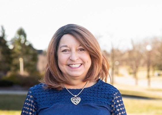 A smiling woman stands outside on a sunny day.