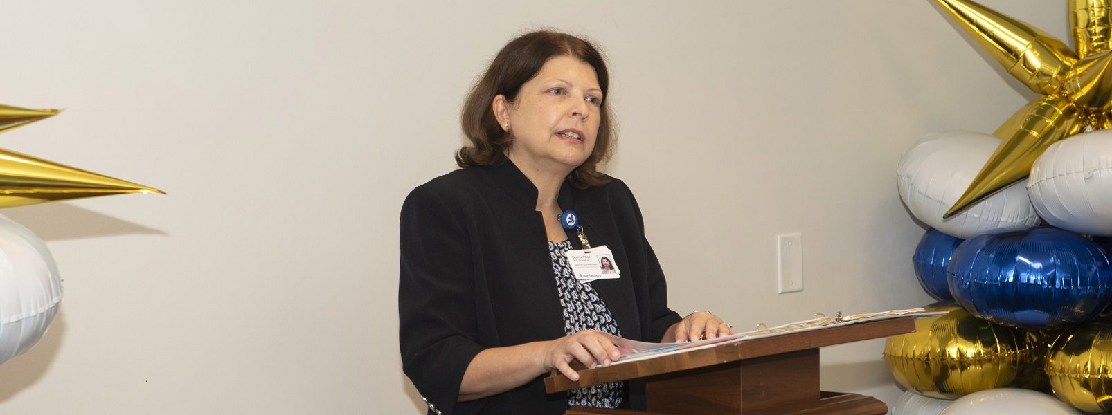 A businesswoman with short, dark hair gives a speech from a podium.