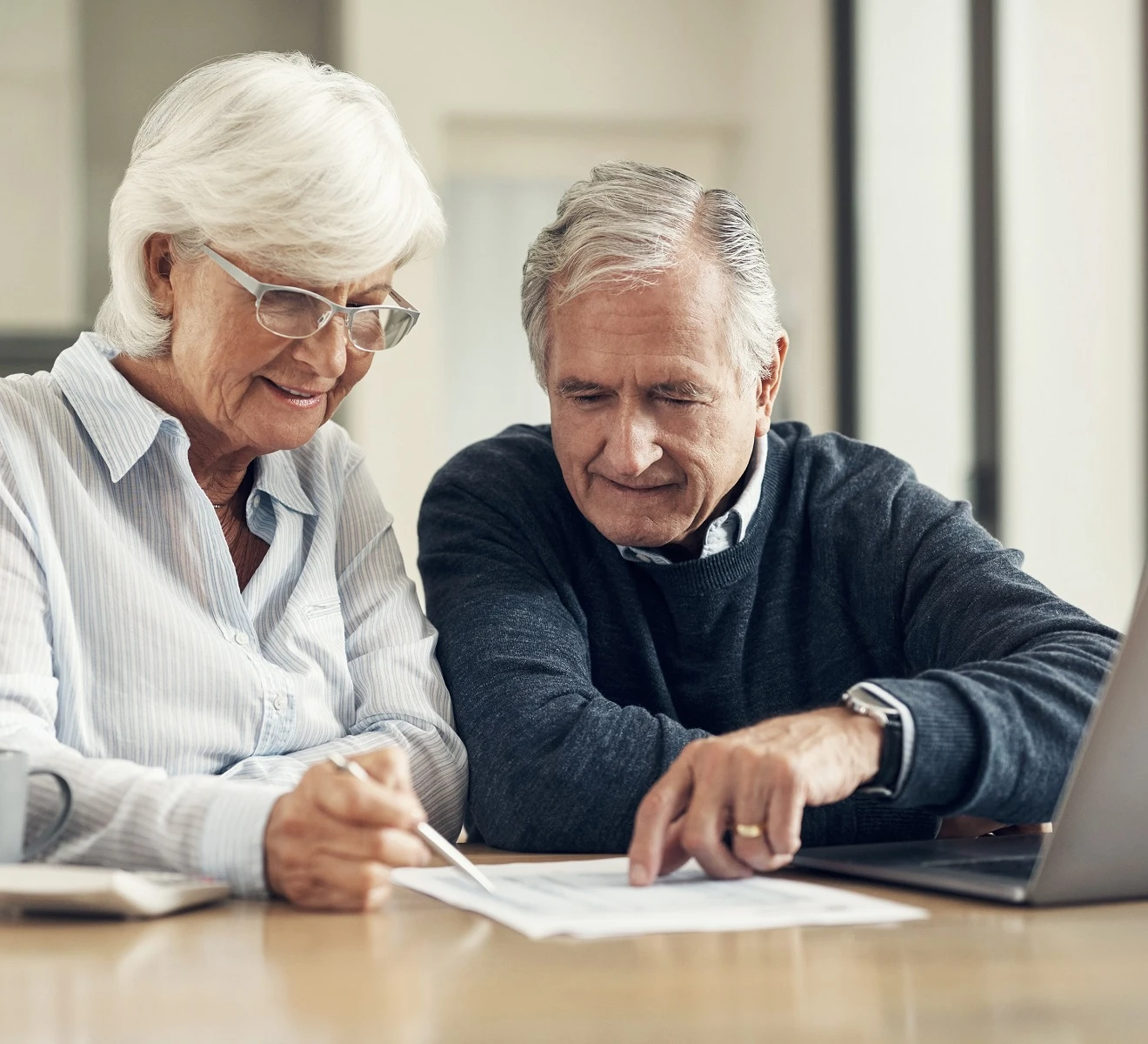 A senior couple sits together at a table, reviewing paper documents.