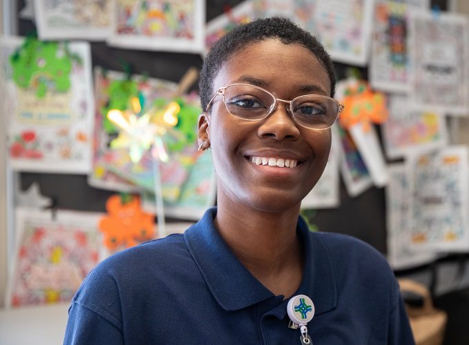 A young woman smiles for the camera while standing in front of a bulletin board.