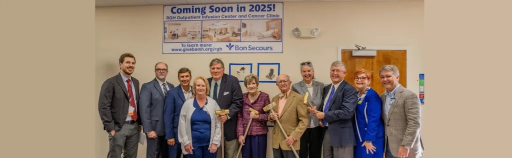 A group of people in suits, hospital scrubs, and construction safety gear line up in front of a wall for a photo.