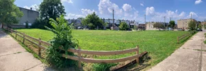 A vacant, overgrown lot in West Baltimore prepared for development. It is a mid-summer day with the sun shining and the grass is green.