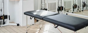 A wide, black table for physical therapy sits in a sunny, clean room.
