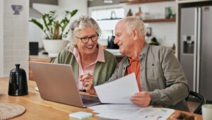 Smiling elderly couple sitting in front of a laptop computer with a paper in hand