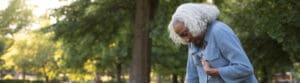 Elderly woman leaning onto park bench while holding her chest
