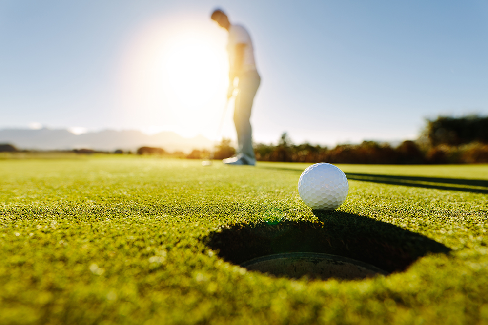 Pro golfer putting golf ball in to the hole. Golf ball by the hole with player in background on a sunny day