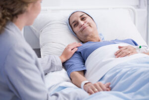 Elderly woman in hospital bed smiling at a visitor who comforts her by holding her hand