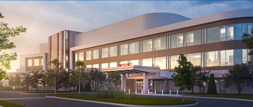 Modern hospital building with the emergency entrance under a canopy, glass walls, and surrounding trees at sunset.
