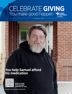 Bearded man in a black hoodie stands outside a brick building with a Celebrate Giving campaign banner above him, conveying support for medication affordability (Samuel).