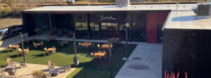 Outdoor dining area in front of Social House with wooden tables on artificial turf.