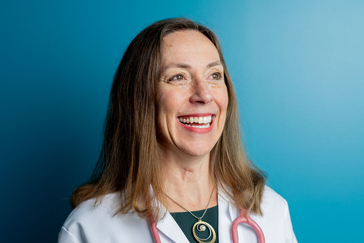 Smiling female doctor in a white coat with a stethoscope against a blue background.