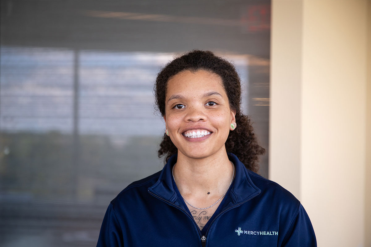 Smiling woman in a navy Mercy Health jacket standing indoors.