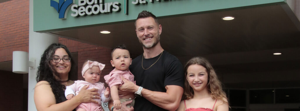 Six-person family posing outside a Bon Secours entrance, smiling at the camera.