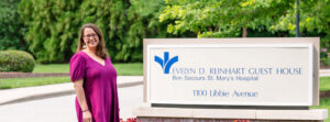 Smiling woman in a magenta dress beside a sign for Evelyn D. Reinhart Guest House, 1100 Libbie Avenue.