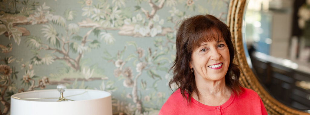 Headshot of Connie Hutson in a wallpapered room with a mirror in the background