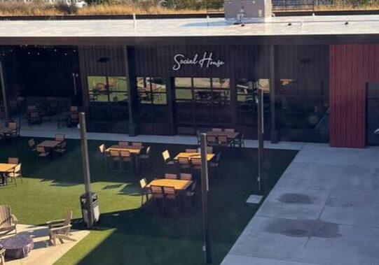 Outdoor dining area in front of Social House with wooden tables on artificial turf.