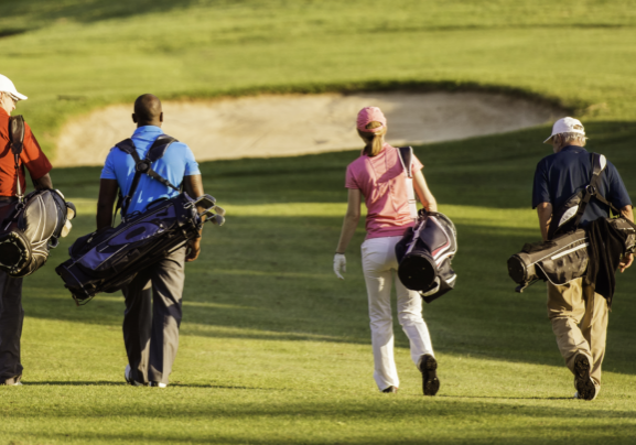 Four golfers of various races, genders and age cross a golf course together.