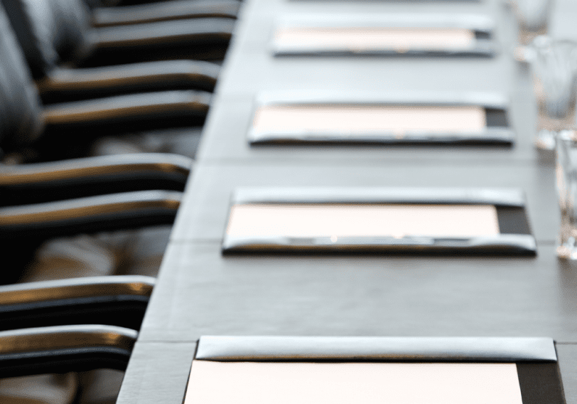 A boardroom table is set with notepads and glasses for water.