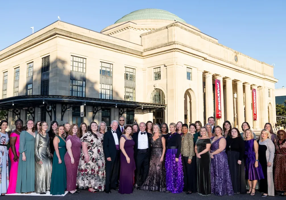 A large group of people dressed in formalwear line up in front of the Science Museum of Virginia for a photo.