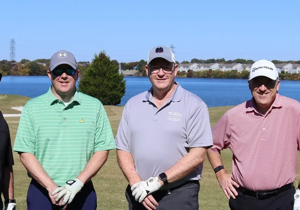 Four men in golf attire lined up on the green, preparing to golf.