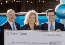 A group of business people, surrounded by balloons, exchange an XL check in front of a hospital under construction.