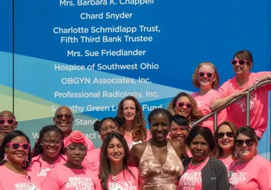 People in bright pink shirts gather together for a group photo in front of a Mercy Health mobile mammography coach.