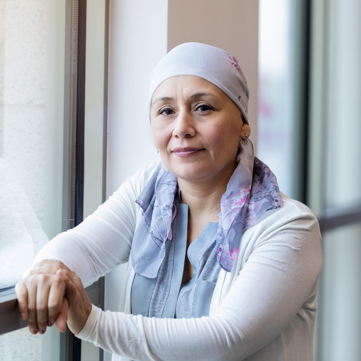 A mid adult woman wearing a scarf poses for a photo for breast cancer awareness month.