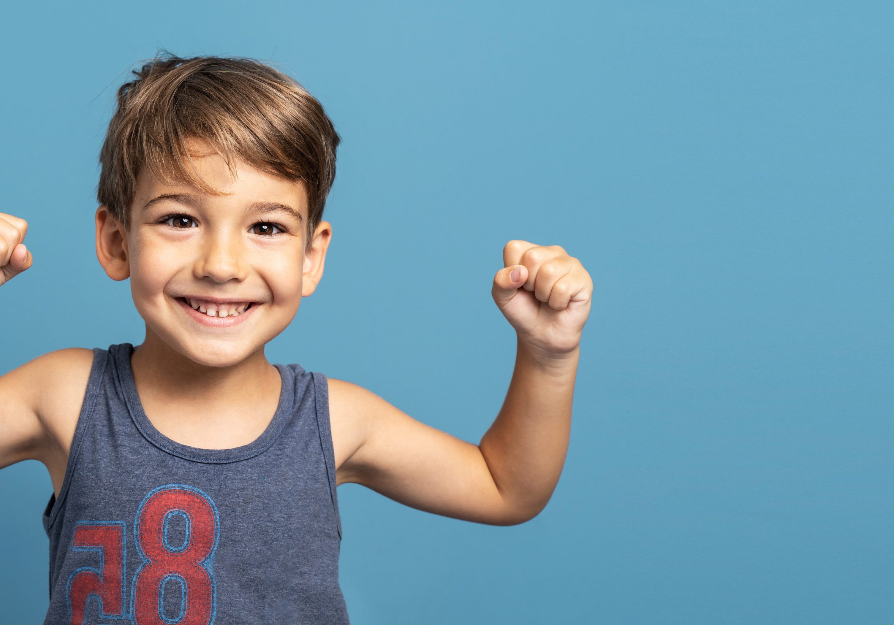 Front view of small caucasian boy four years old standing in front of blue background studio shot standing confident flexing muscles smiling growing up and strength and health concept