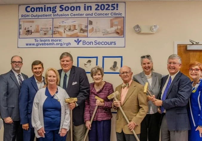 A group of people in suits, hospital scrubs, and construction safety gear line up in front of a wall for a photo.