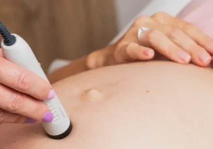 A doctor uses a portable fetal monitor on a pregnant patient's stomach to check the heartbeat of a fetus.