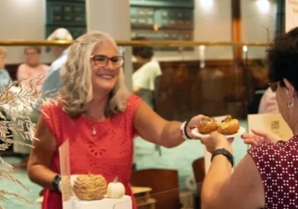 A smiling vendor serves a plate of donuts to a customer at a tasting event.