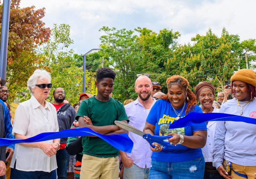 A crowd of people gathers to cut a big, blue ribbon at the opening of Unity Park in Franklin Square, MD.